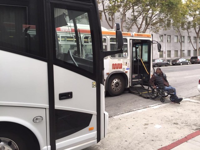 A shuttle bus blocks a Muni stop, forcing a passenger in a wheelchair to get off in the middle of the street